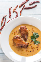 Portion of pea cream soup with smoked chicken wings