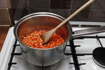 Saucepan of baked beans cooking on a gas oven hob with wooden sp