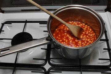 Saucepan of baked beans cooking on a gas oven hob with wooden sp