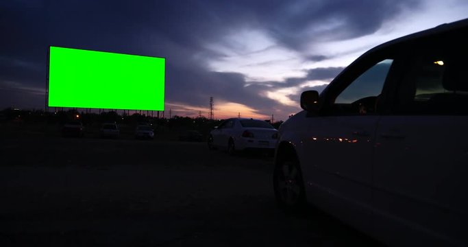 Wide shot of blank drive in movie screen with car at dusk