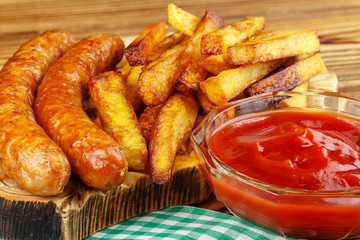 Homemade fast food, portion of french fries, ketchup, grilled sausages, on wooden board.