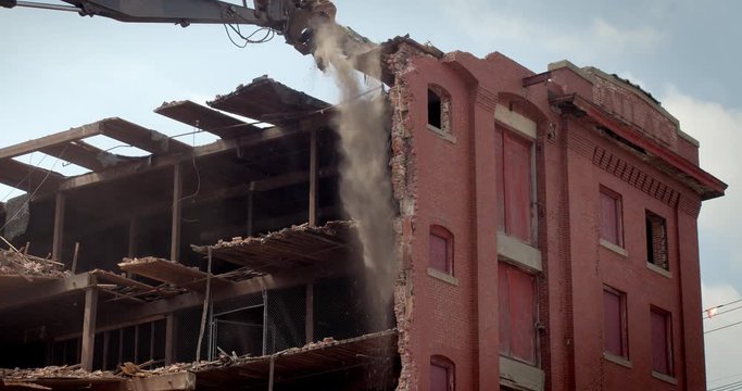 Wide shot of excavator demolishing brick building