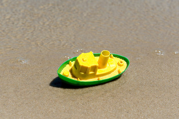 Fototapeta na wymiar Toy boat in the wet sand of the sea. Summer holidays at sea. Boat trips.