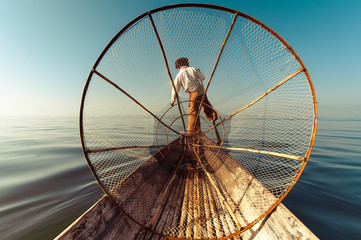 Burmese fisherman on bamboo boat catching fish in traditional way with handmade net. Inle lake,...