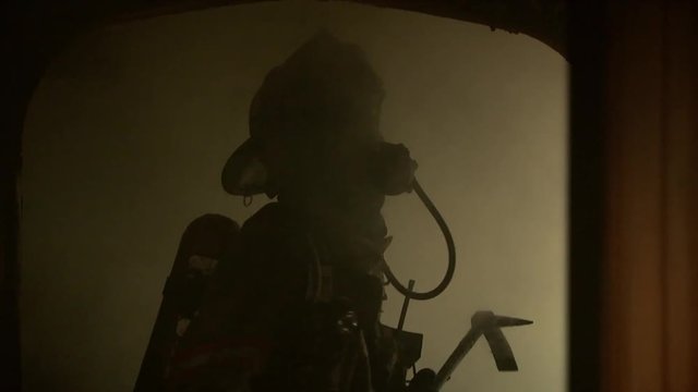 Zoom in shot of a firefighter in smoldering house
