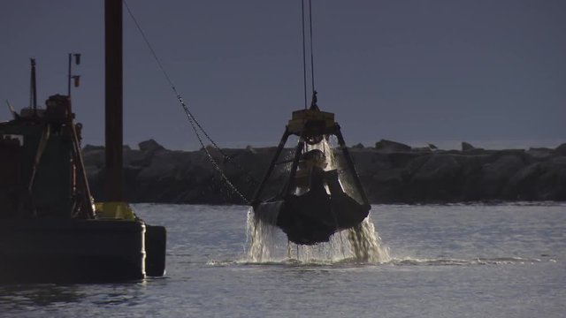 Tracking shot of industrial crane dredging in harbor