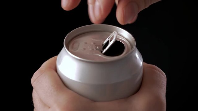 Close up of a hand opening a beverage in aluminum can. Isolated on black.