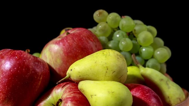 Heap of delicious fruits (apples, bananas, green grapes and pears) rotating on black background. Loop