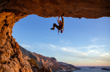 Male climber on overhanging rock against beautiful view of coast below 