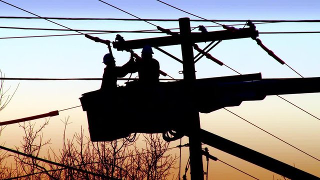 Utility workers working on powerline during sunset