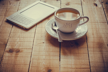 A cup of tea and an ebook reader on a rustic wood table