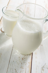 fresh milk in glass jug and glass on wooden background