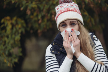 Pretty young woman blowing her nose with a tissue outdoor