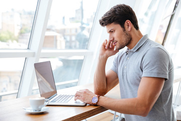 Handsome pensive man working with laptop while having coffee break