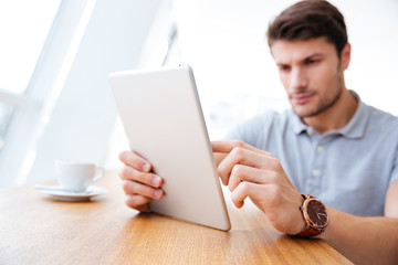 Attractive businessman in casual clothes using tablet and drinking coffee