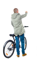 back view of pointing man with a bicycle. Cyclist in parka jacket keeps the wheel of a bicycle. Rear view people collection.  backside view of person. Isolated over white background.