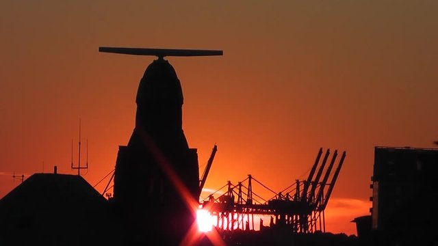 Pegelturm an den Landungsbr&uuml;cken und Hafenkr&auml;ne im Hamburger Hafen bei Sonnenuntergang