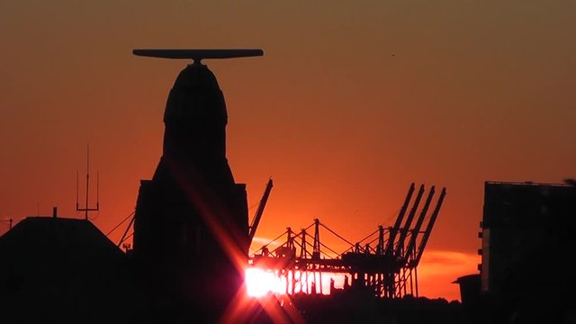 Pegelturm an den Landungsbr&uuml;cken und Hafenkr&auml;ne im Hamburger Hafen bei Sonnenuntergang