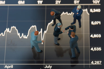 Top view selective focus of miniature businessman handshake with against stocks and shares as commitment, partnership, business and investment concept.