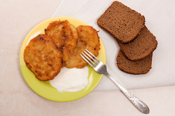Potato pancakes with meat and sour cream on green plate with rye