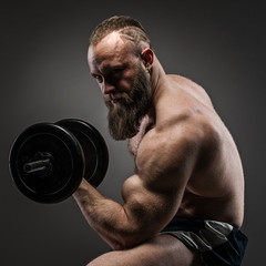 Muscular bearded bodybuilder guy doing exercises with dumbbells.
