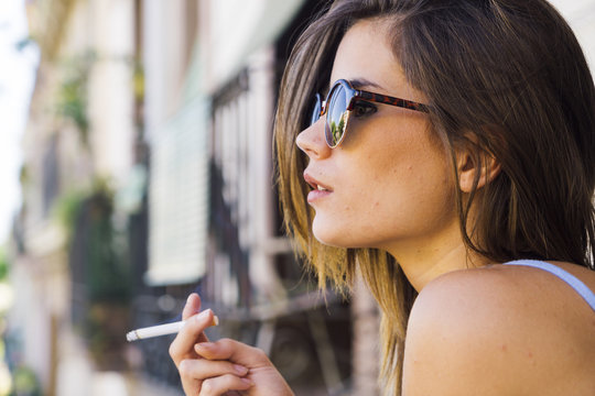 Beautiful young girl in sunglasses smoking cigarette