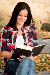 Beautiful young woman reading a book in park at fall