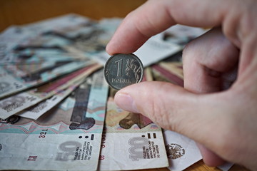 Male hand holding a Russian coin (Russian Ruble, RUB) with a background created of Russian bank notes in the shape of circle 