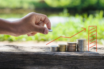 hand putting coin in increasing stack of money coins, saving money and sunshine
