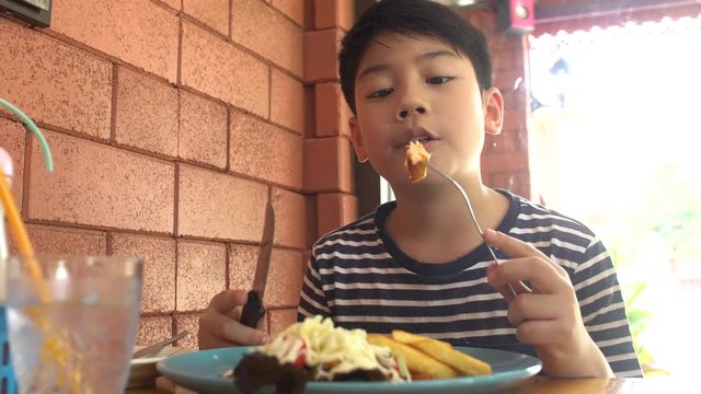 Little asian child eating pork steak at restaurant ,happy asian boy enjoy at your meal.
