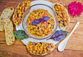 Roasted eggplant and tomatoes hot salad with basil, sandwiches with vegetable pate on wooden background