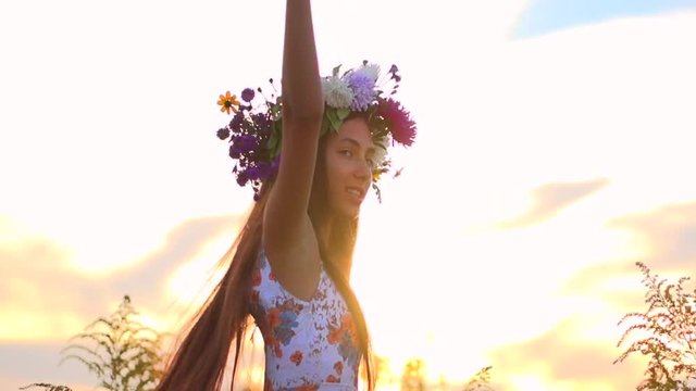 Beautiful girl with flower wreath on her head. Happy girl with flowers on  head spinning in a meadow.  Slow motion 240 fps.
