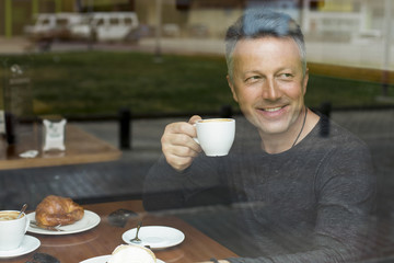 Attractive smiling mid adult man drinking morning coffee in cafe