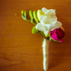 White boutonniere with pink flower lies on the wooden table