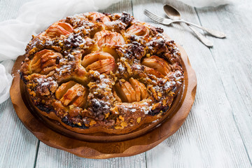 Homemade sweet fruit cake on wooden board. Made with whole partially sliced apples, walnuts,...