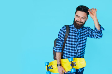 Hipster man over colorful blue background holding yellow skateboard