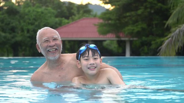 Happy asian family playing in pool, Asian grandchildren and grand parents swimming in pool.