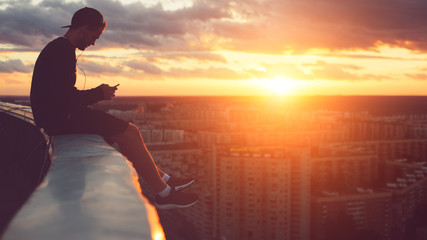 Young risky man chilling above the city with smartphone at sunset