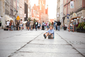 a little blond boy sitting on a ground in a city center