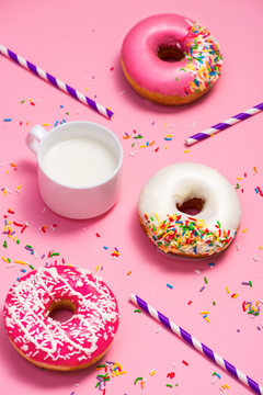 Donuts with icing and milk on pastel pink background. Sweet donu