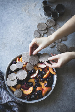 A hand placing dough shapes on a blackberry peach buckwheat pand