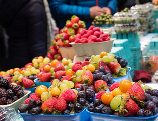 Miscellaneous berries on sale on a country farm market with buyers on a background