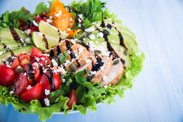 Fresh salad plate with colorful tomatoes, chicken, cheese, avocado, lime, balsamic mousse and mixed greens on wooden background. Healthy food. Nutritious meal.