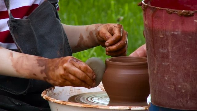 Pottery Process. Potter Smoothing the Surface of Cley Pot With the Round Stone. Throwing Wheel Speaning, Assistant Helping, Raw Material on the Side