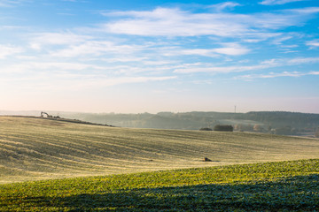 The first frost in the fields. Misty autumn morning. On the horizon the area of road investments.
