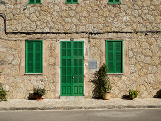 Gröna fönsterluckor och dörr på hus med stenfasad