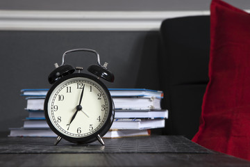 Naklejka premium Black alarm clock on a black and white striped napkin showing 7 o'clock on a bedside table