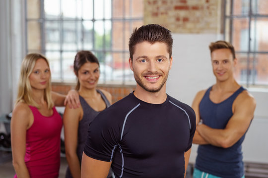 lächelnder mann im fitnesstudio mit team im hintergrund