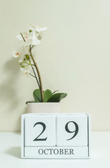 Closeup white wooden calendar with black 29 october word with white orchid flower on white wood desk and cream color wallpaper in room textured background , selective focus at the calendar