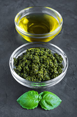 Pesto and olive oil in glass bowls and fresh basil leaves